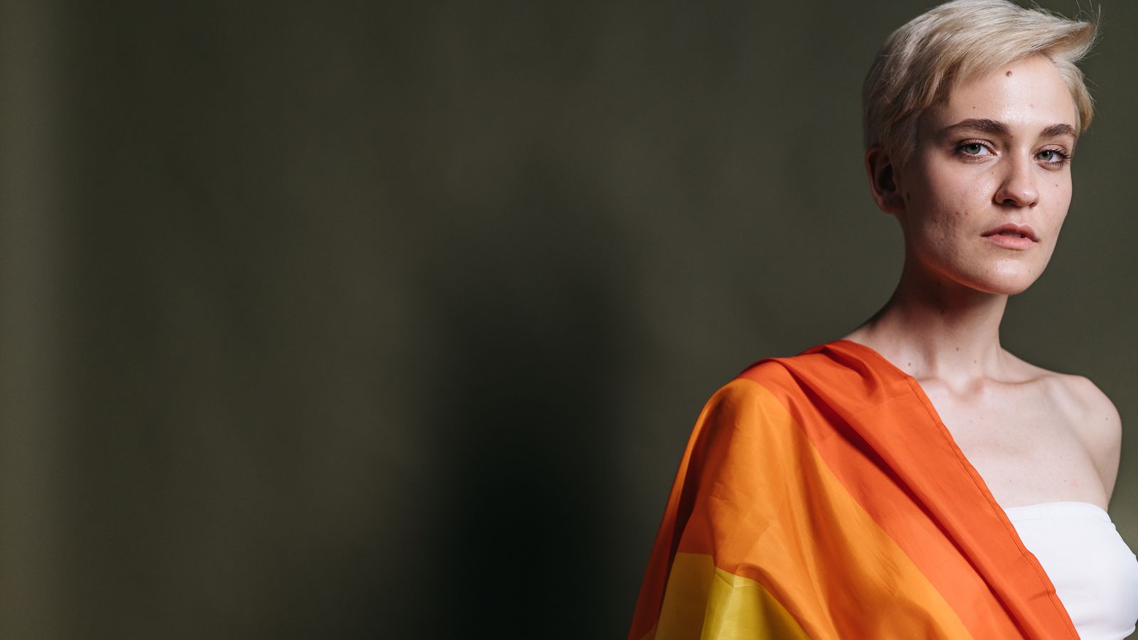 Adult with a rainbow flag draped over one shoulder, representing trans women navigating androgenetic alopecia
