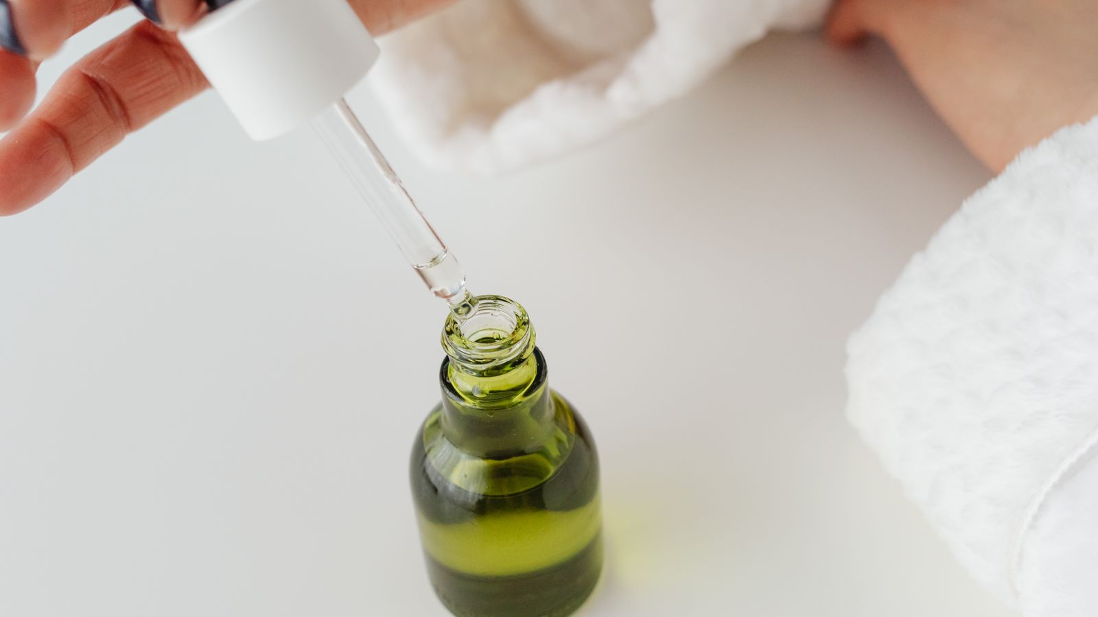 Hands holding a dropper over a green serum bottle, illustrating whether expensive serums are worth it