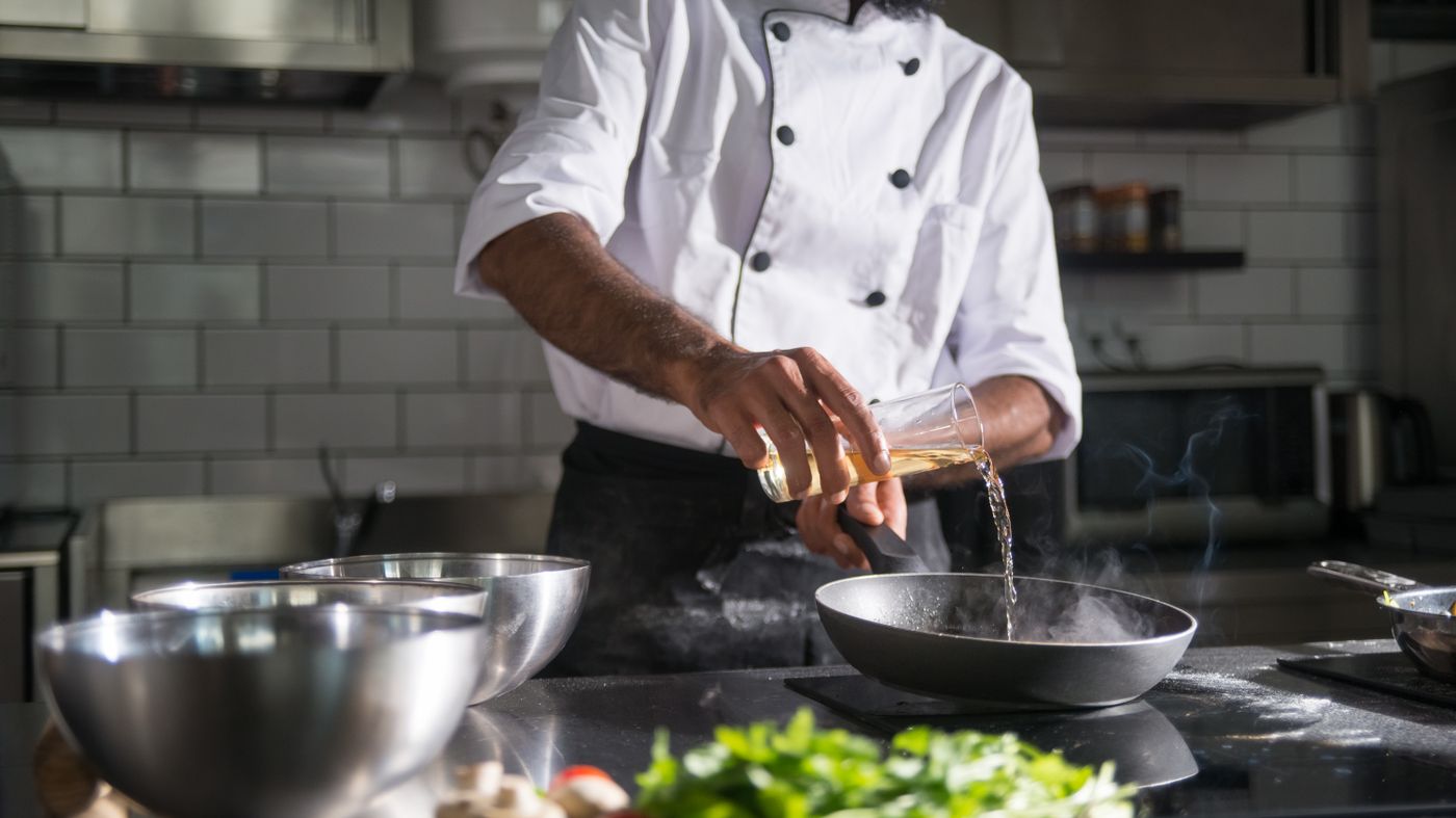 Chef pouring cooking oil into a frying pan, illustrating the question of whether seed oils are bad for you