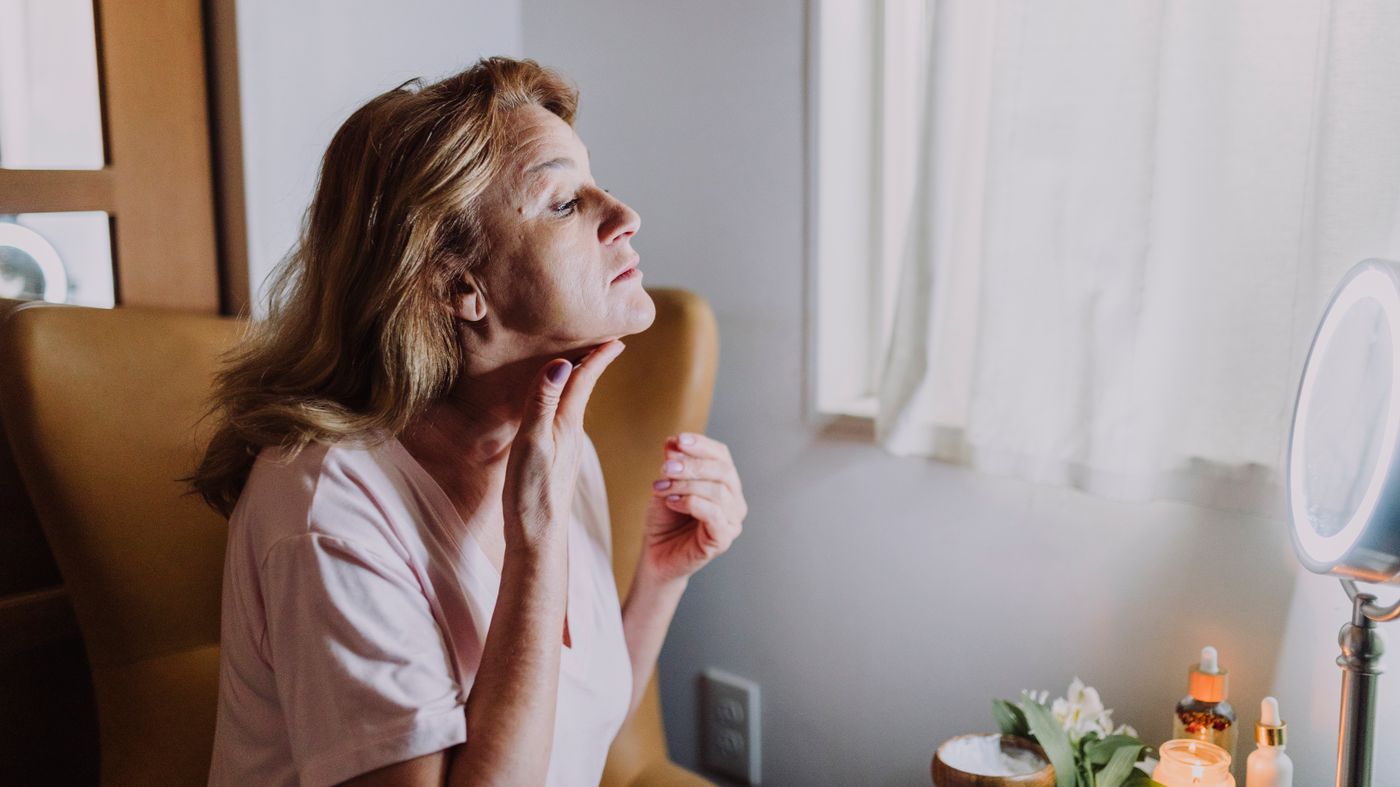 Mature woman examining her skin beside skincare products while choosing the best anti ageing ingredients