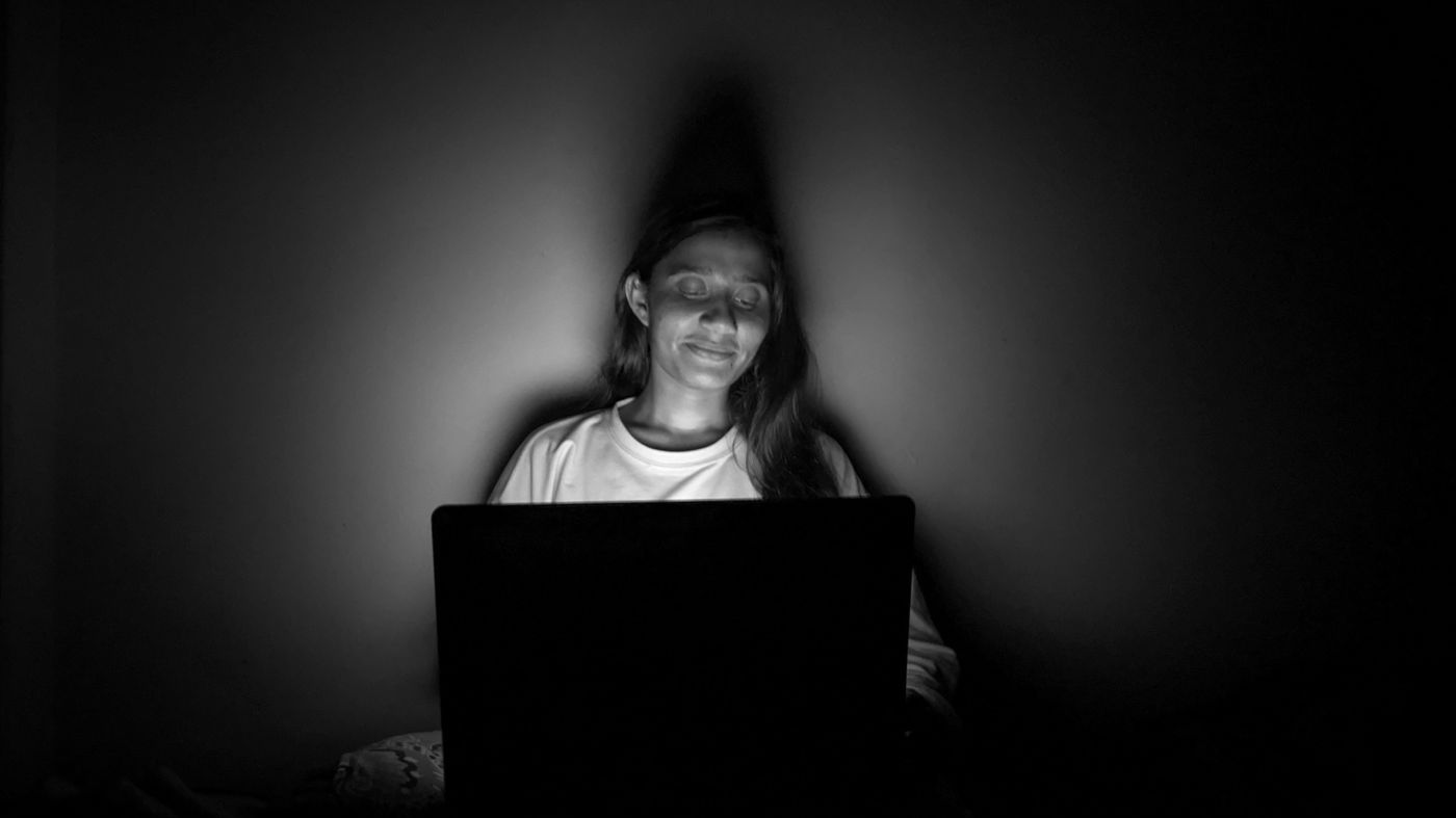 Woman lit by a laptop screen at night, the usual worry about blue light skin damage
