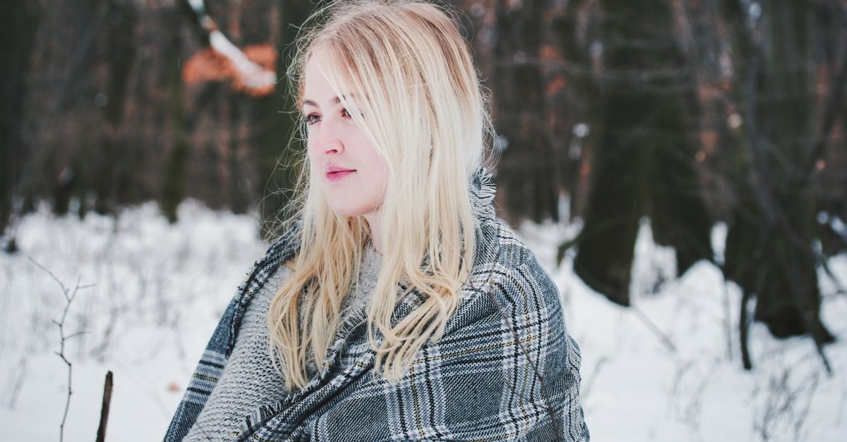 Woman wrapped in a scarf in a snowy forest, cold air is a main cause of dry skin in winter