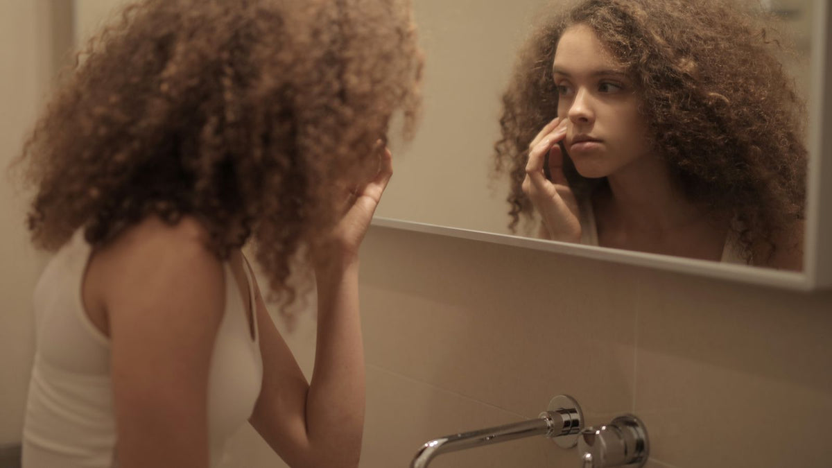 Young woman checking her hair and parting in a bathroom mirror, wondering about follicle dormancy