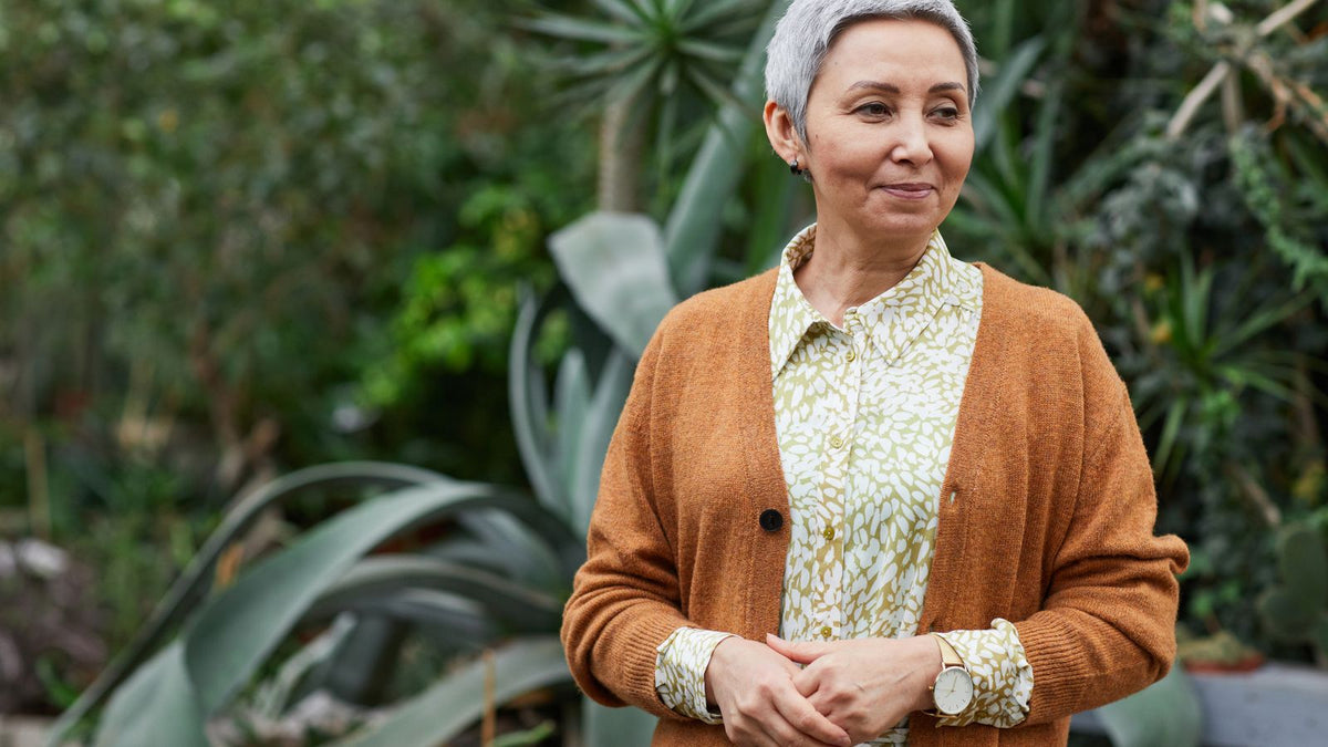 Smiling older woman with short hair in a garden, thinking about her hair after stopping HRT