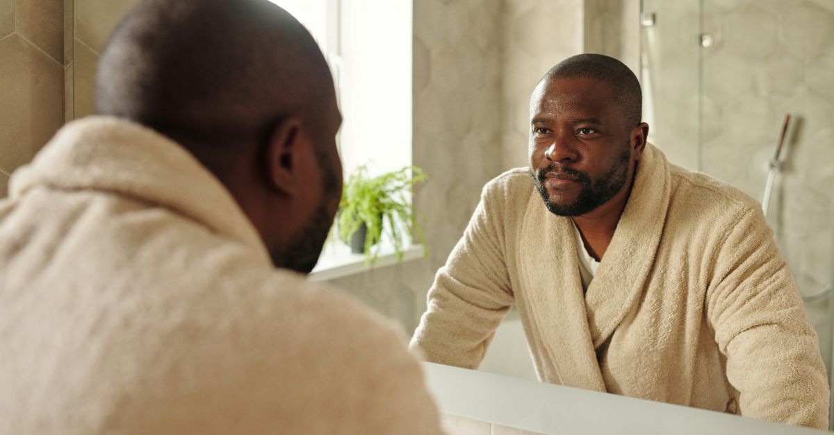 A man studying his reflection in a bathroom mirror, where hair care for genetic thinning usually begins