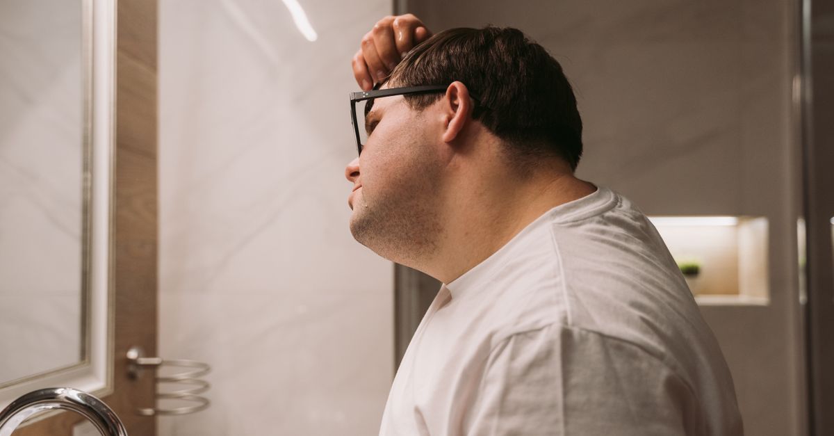 Man checking his hairline in a bathroom mirror for signs of hair follicle miniaturisation