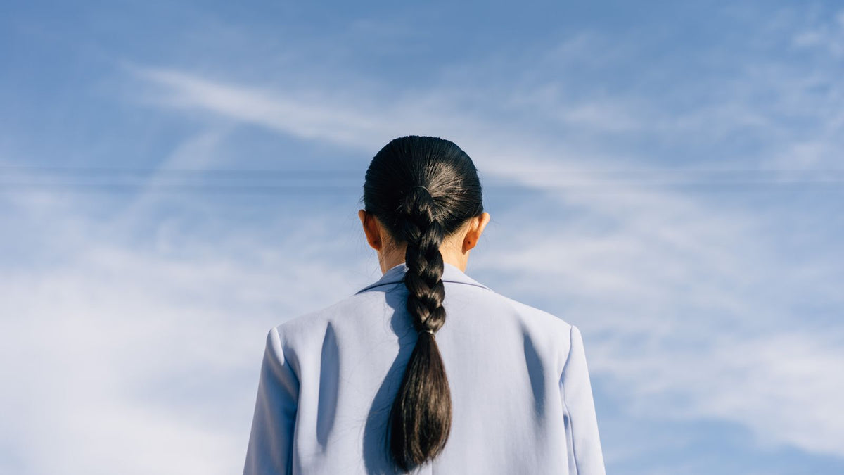 Back view of a teenager with a long braid, the everyday styling behind hair loss in teenagers