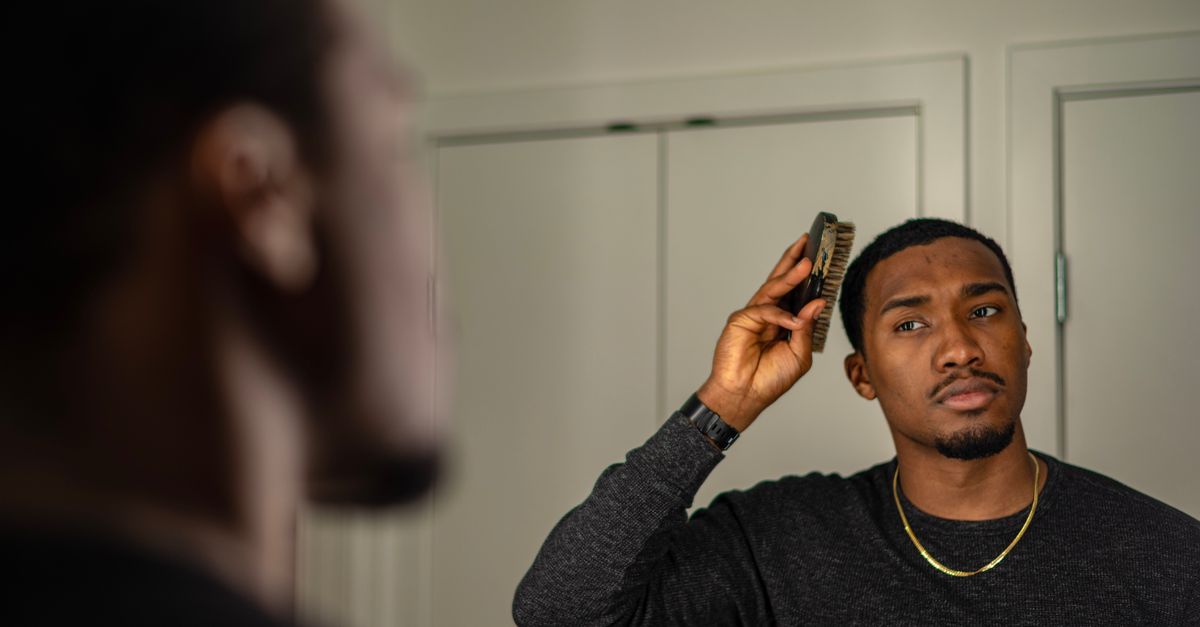 Man checking his hairline in the mirror while combing, a common first sign of hair loss on testosterone
