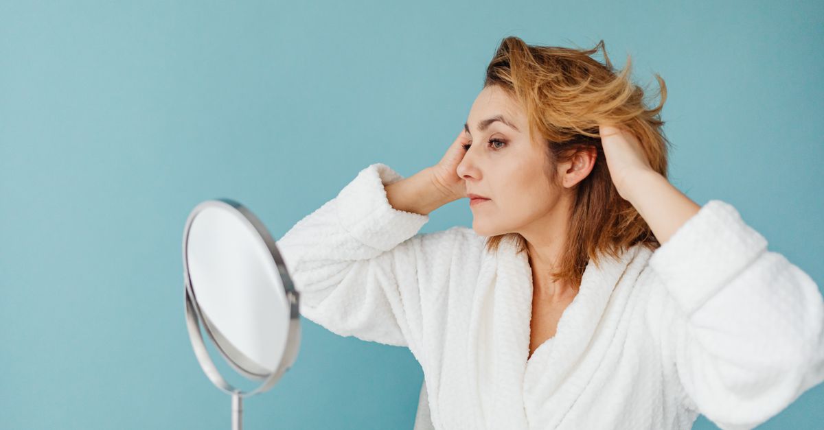 Woman examining her hair in the mirror after noticing hair thinning