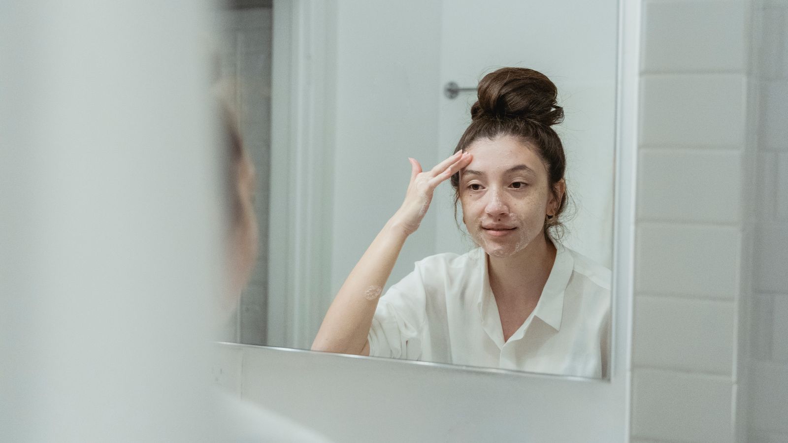 Woman applying face cream at the mirror, where skincare meets the hairline