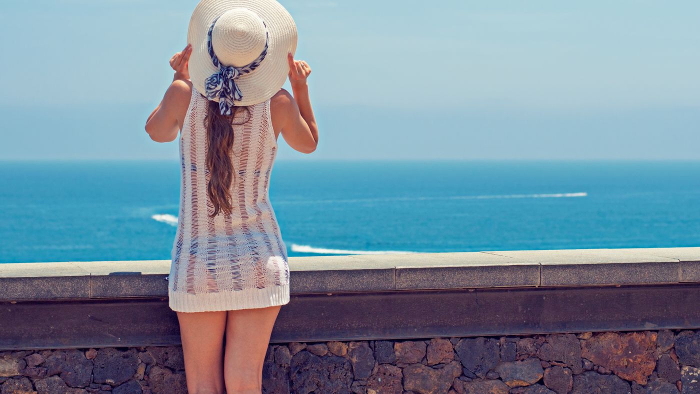 Woman in a wide brimmed sun hat by the sea, shade is the simplest holiday hair care step