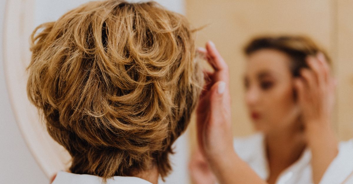 Woman checking her parting in the mirror for signs of hormonal hair thinning