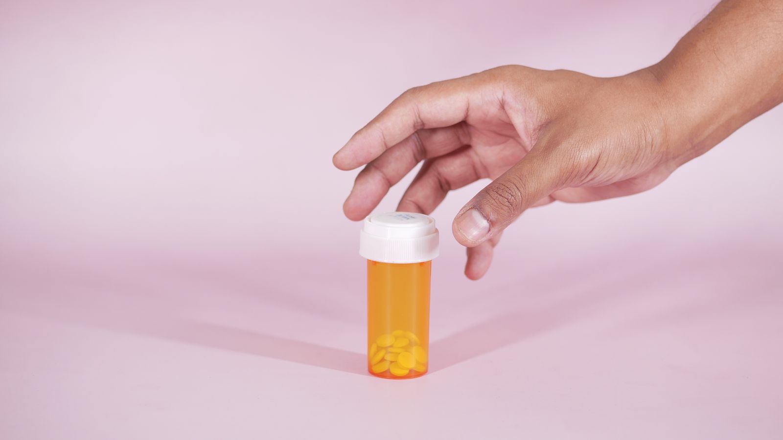 Hand reaching for a prescription bottle, reflecting the medicines involved in hormone therapy hair loss