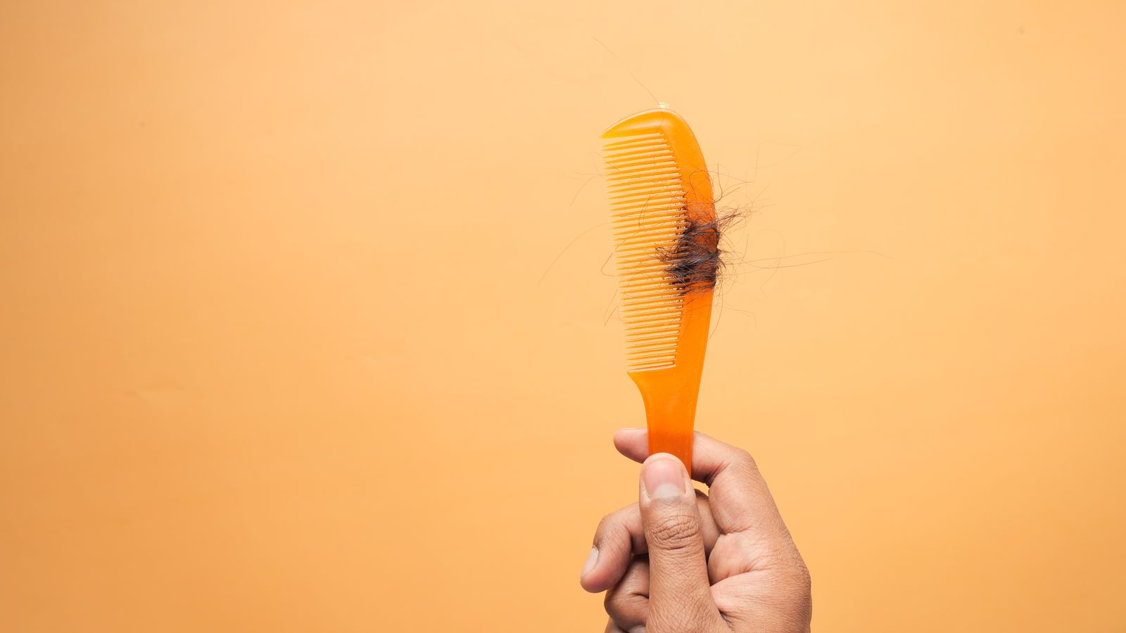 Hand holding a comb with loose strands, a familiar sight during hormone therapy hair shedding