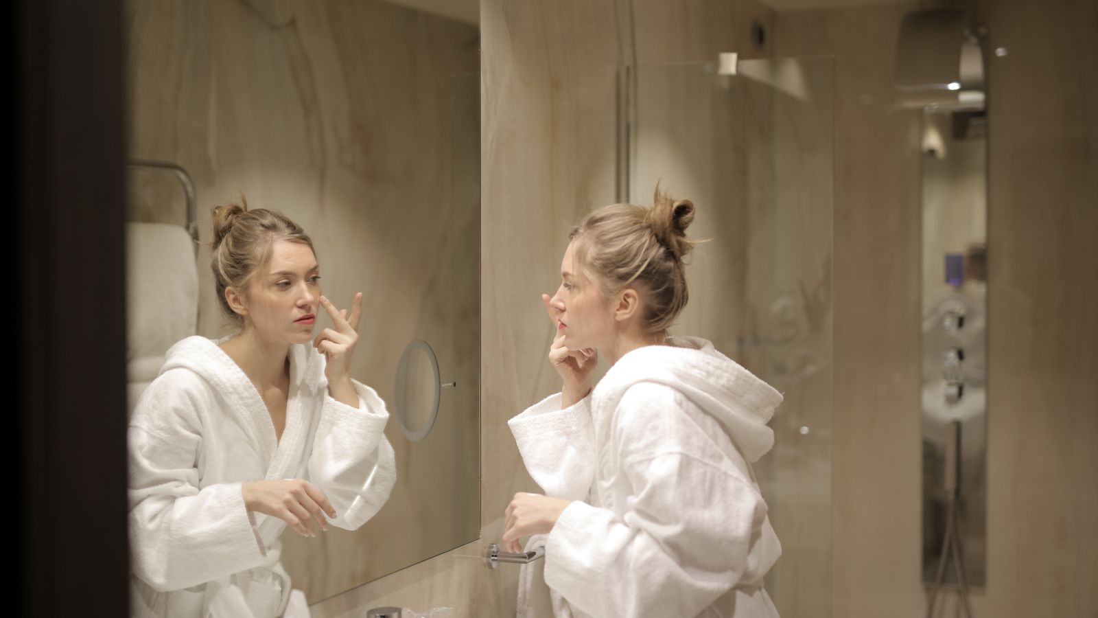 Woman applying product to her face at a bathroom mirror, showing how to apply sunscreen on oily skin