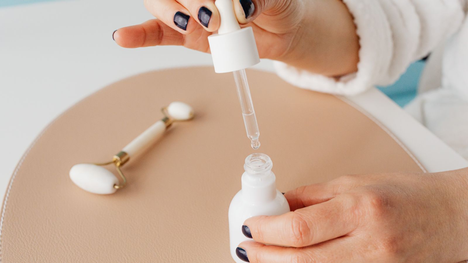 Hands holding a serum dropper beside a jade roller, showing how to use snail mucin