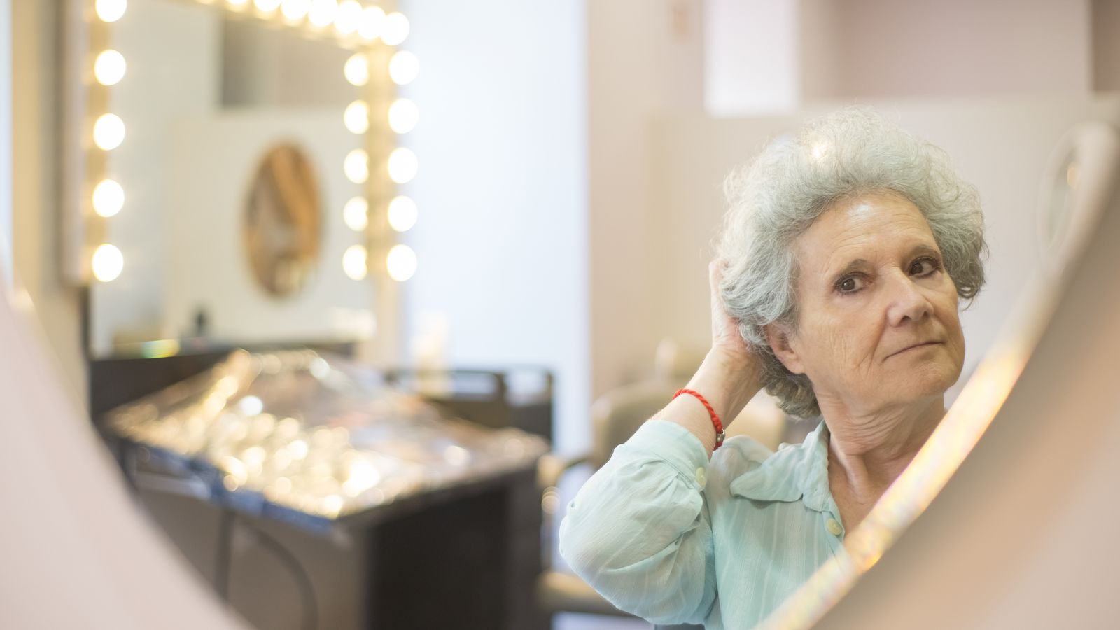 Woman adjusting her hair in a mirror, reviewing her HRT hair care routine