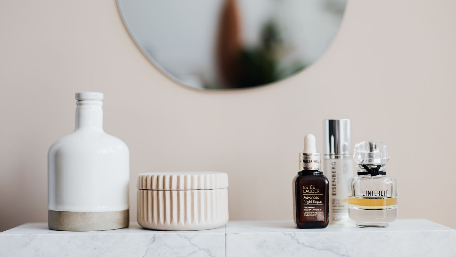 Cream and lotion bottles arranged on a marble surface, illustrating the luxury vs drugstore skincare decision