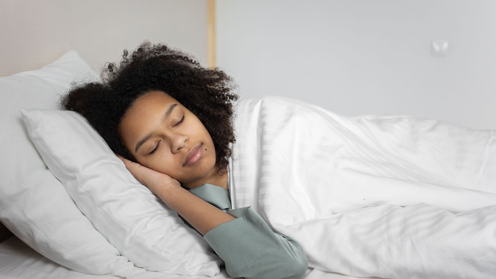 Woman sleeping peacefully in bed, the sleep link behind melatonin for hair growth