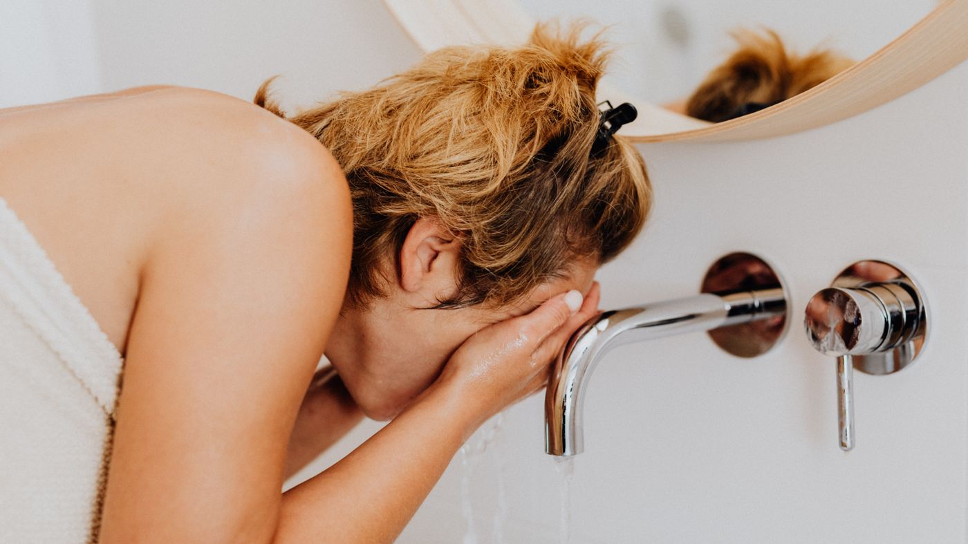 Woman washing her face at a sink as part of microbiome friendly skincare