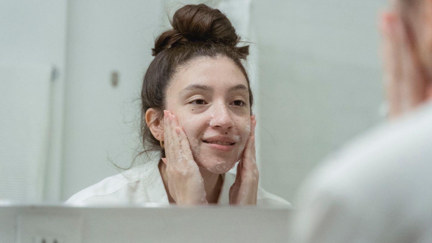 Woman applying a light moisturiser for oily skin at the bathroom mirror