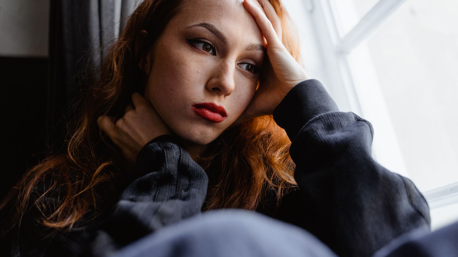 Young woman looking out of a window, thinking through what pcos hair loss means for her