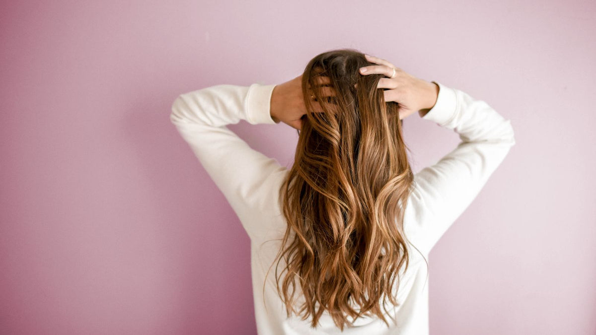 Back view of a woman with long brown hair, the scalp beneath fed by scalp microcirculation