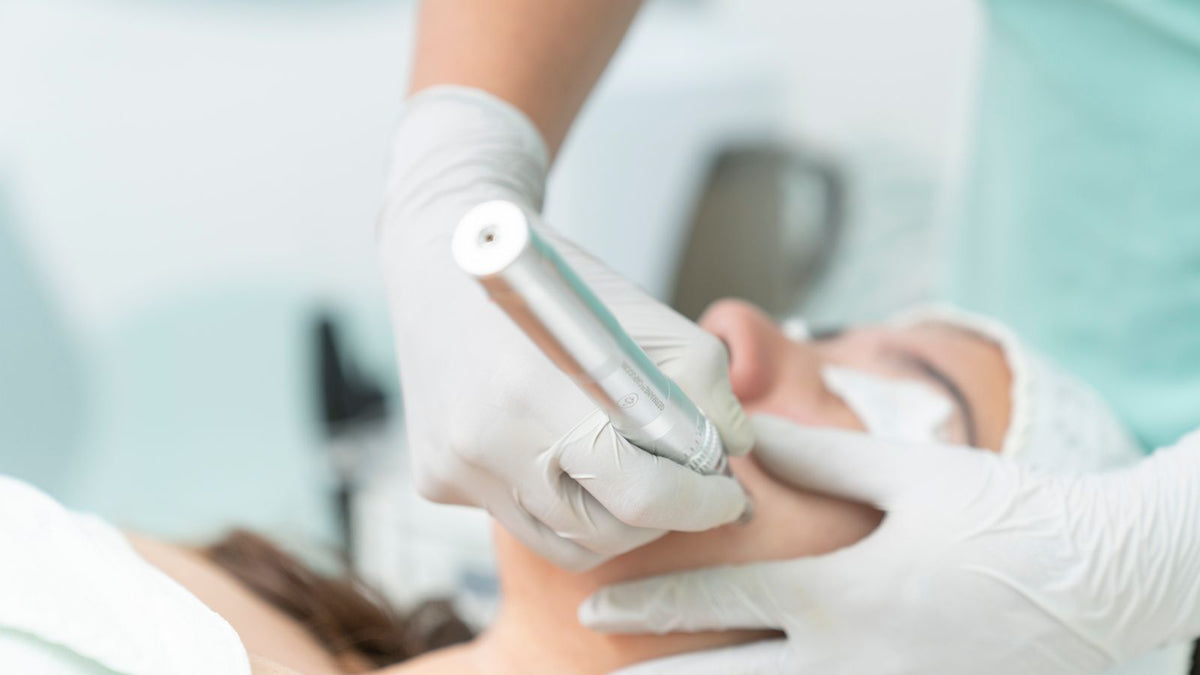 A microneedling pen being used by a gloved practitioner in a clinic, the device type also used for scalp microneedling