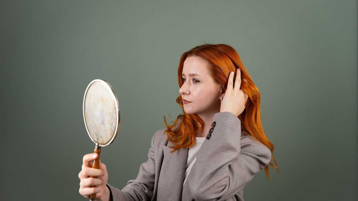 Woman with red hair holding a mirror, checking for signs of new hair growth