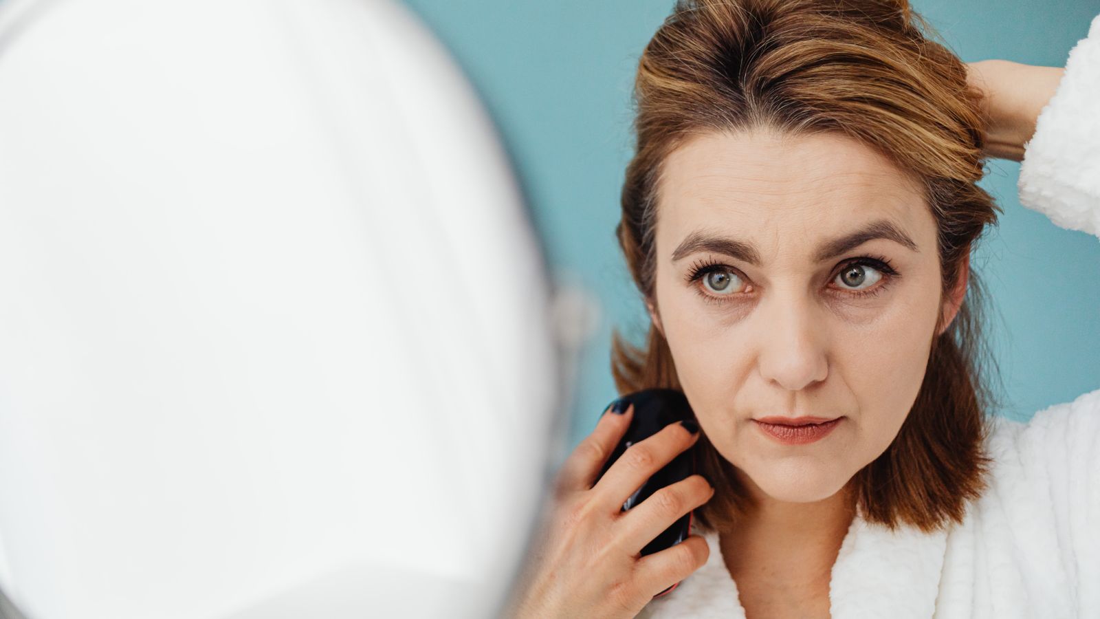 Woman styling her hair at a mirror, working through simple solutions thinning hair responds to