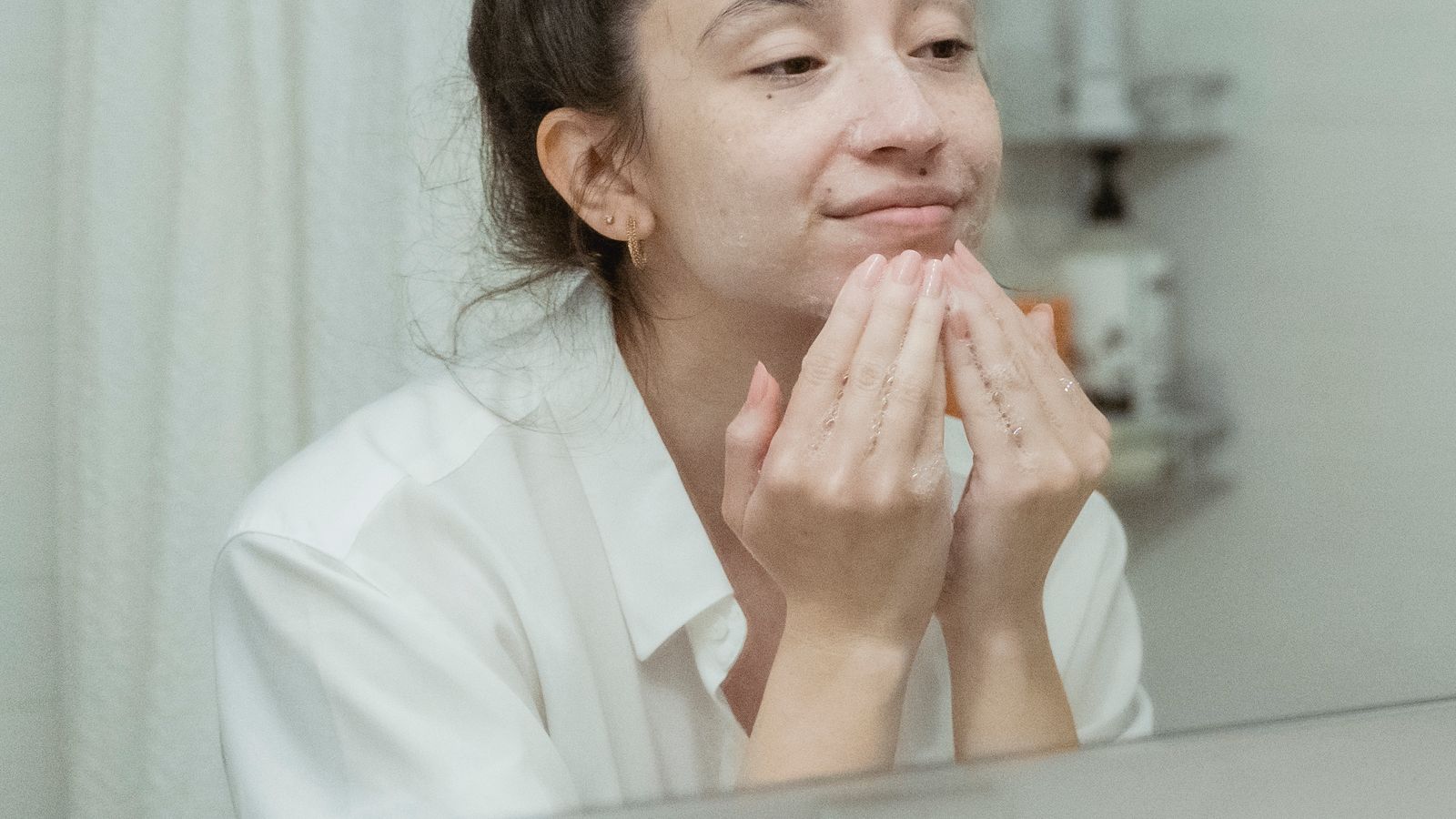Woman applying face cream at a bathroom mirror, illustrating the hard truths about a skincare routine