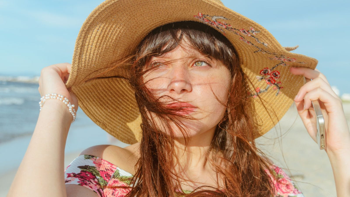 Woman in a straw hat on a sunny beach, the first line of summer hair care