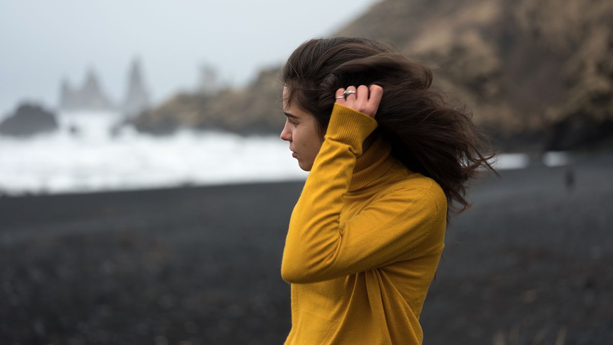 Woman with long hair on a cold, windy rocky shore, the weather behind many trichologist Aberdeen questions about dry hair