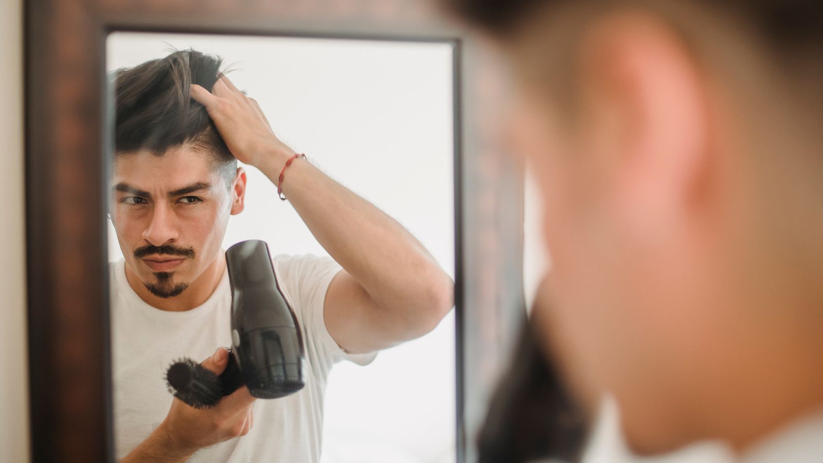 Man styling his hair at the mirror and checking his hairline, the first step before seeing a trichologist in Harrow