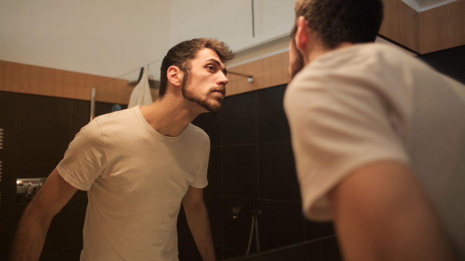 Man checking his hairline in a bathroom mirror before seeing a trichologist in Hillingdon