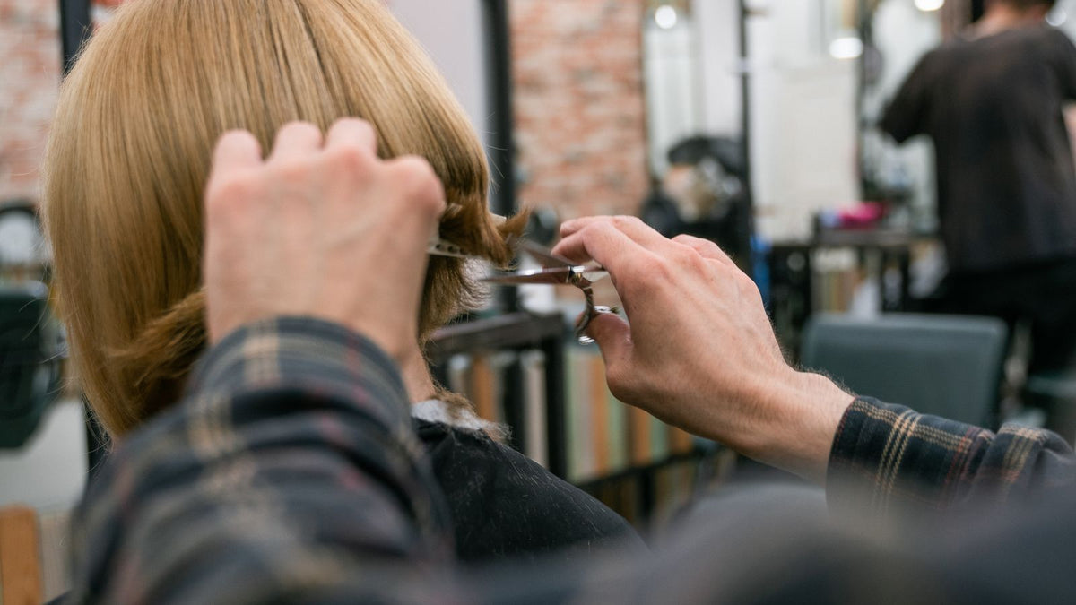 Hairdresser cutting a woman's blonde hair to a fuller-looking length, for readers looking for a trichologist in Crawley