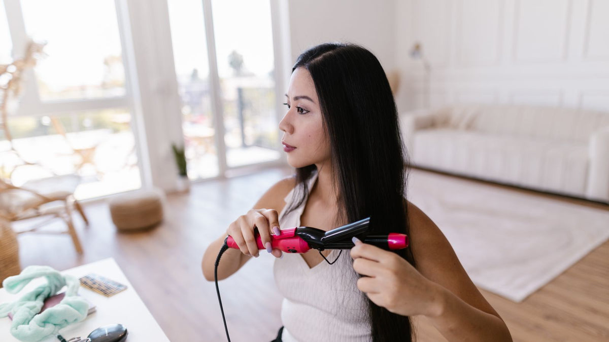Woman using a flat iron on dry hair at home, the kind of daily heat styling people ask a trichologist in Hemel Hempstead about