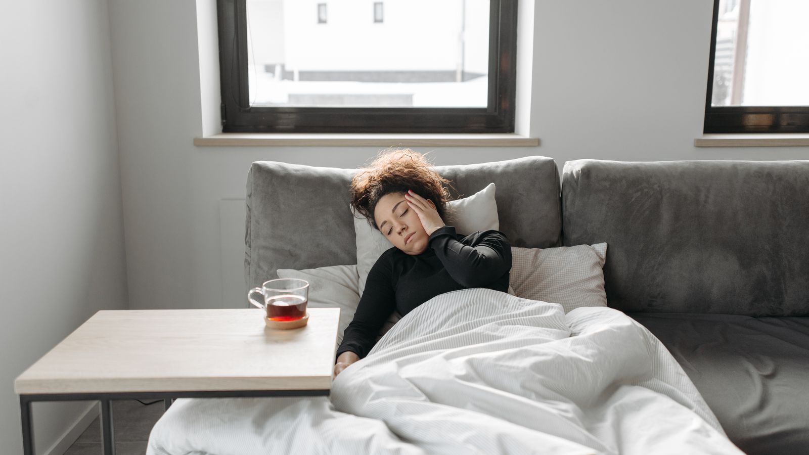 Woman resting on a couch with tea while unwell, the kind of illness a trichologist in Penrith links to shedding months later