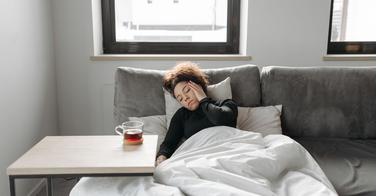 Woman resting unwell on a sofa with tea, the illness a trichologist in Penrith links to hair shedding months later