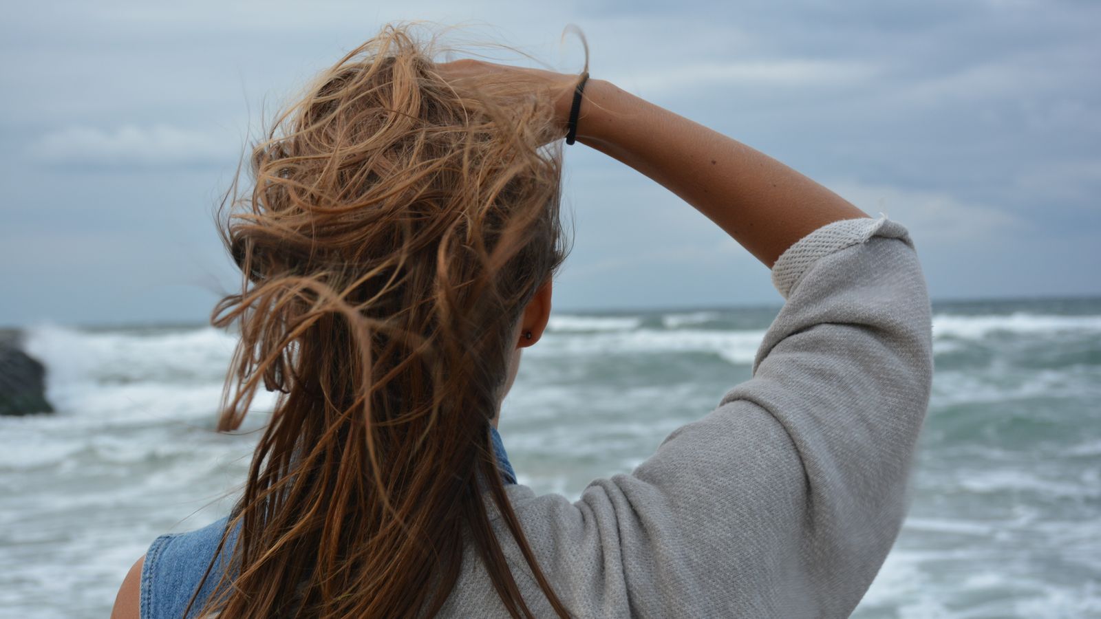 Woman with wind tousled hair looking out at the sea, coastal hair care and trichologist advice in Skegness