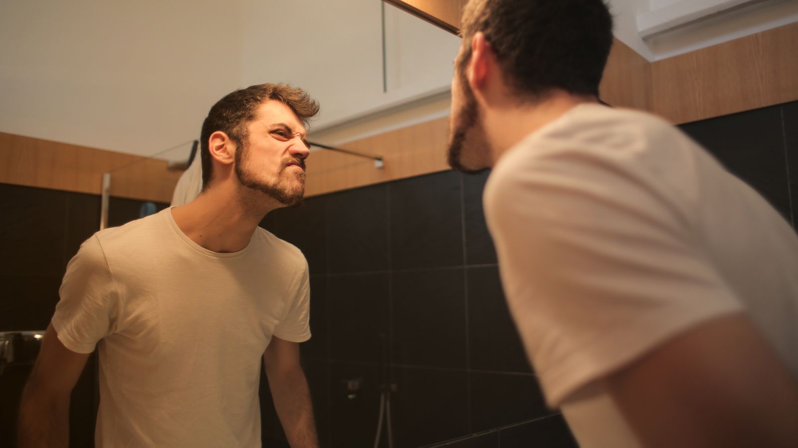 Man studying his hairline in a bathroom mirror before booking a trichologist in Wandsworth