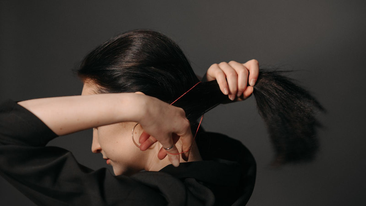 Close-up of a woman tying her hair with a rubber band, the habit trichologists Braintree say snaps fine hair