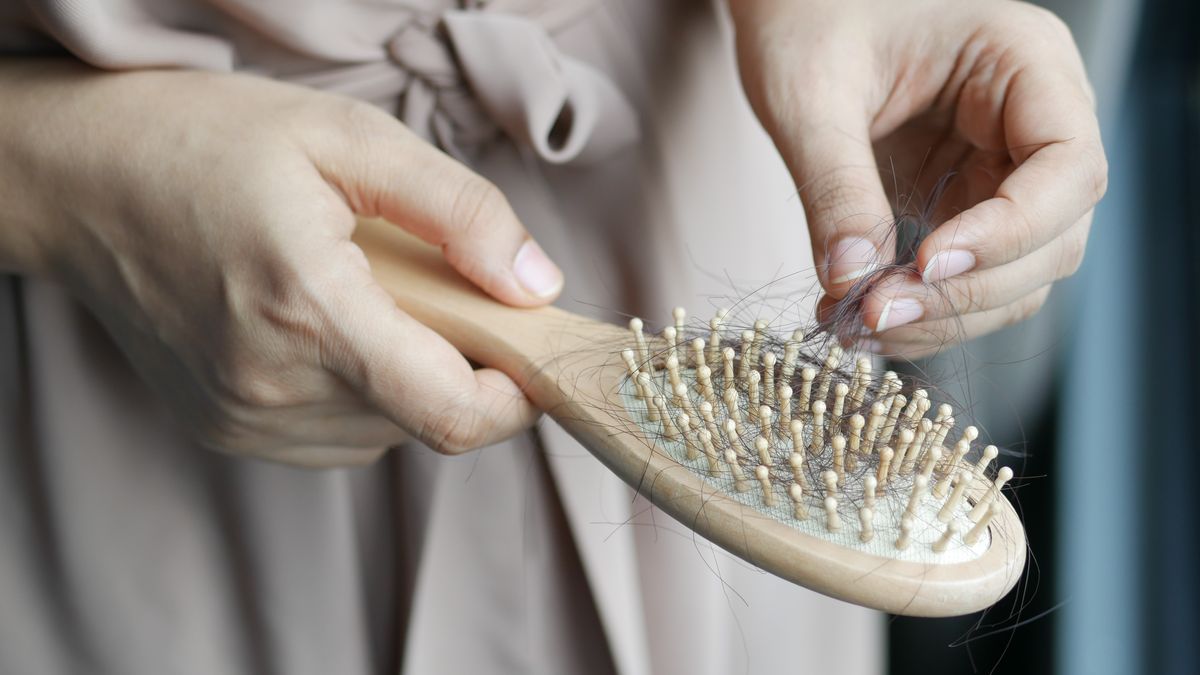 Hands pulling shed hairs from a wooden hairbrush after an illness, a common reason people look for trichologists Derby