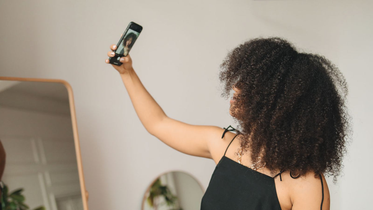 Woman photographing her hair parting in a mirror at home, the first step in preparing for trichologists Greenock appointments
