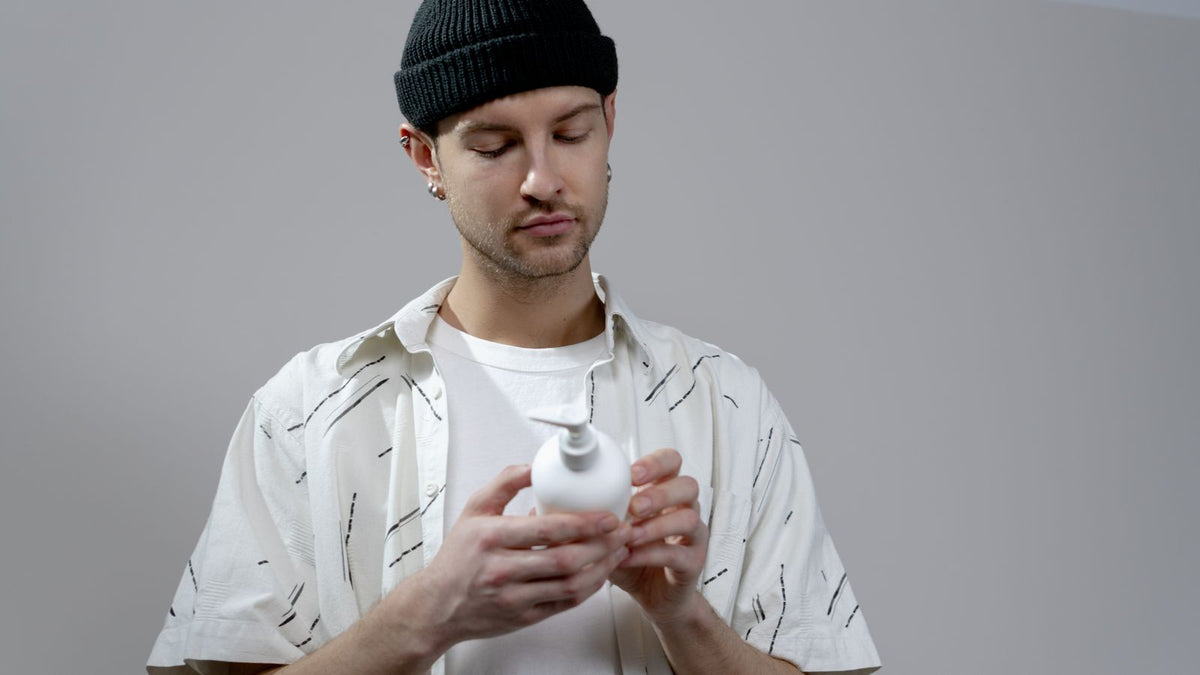 Man reading the label on a white shampoo bottle, the first step before contacting trichologists Newport about thinning hair