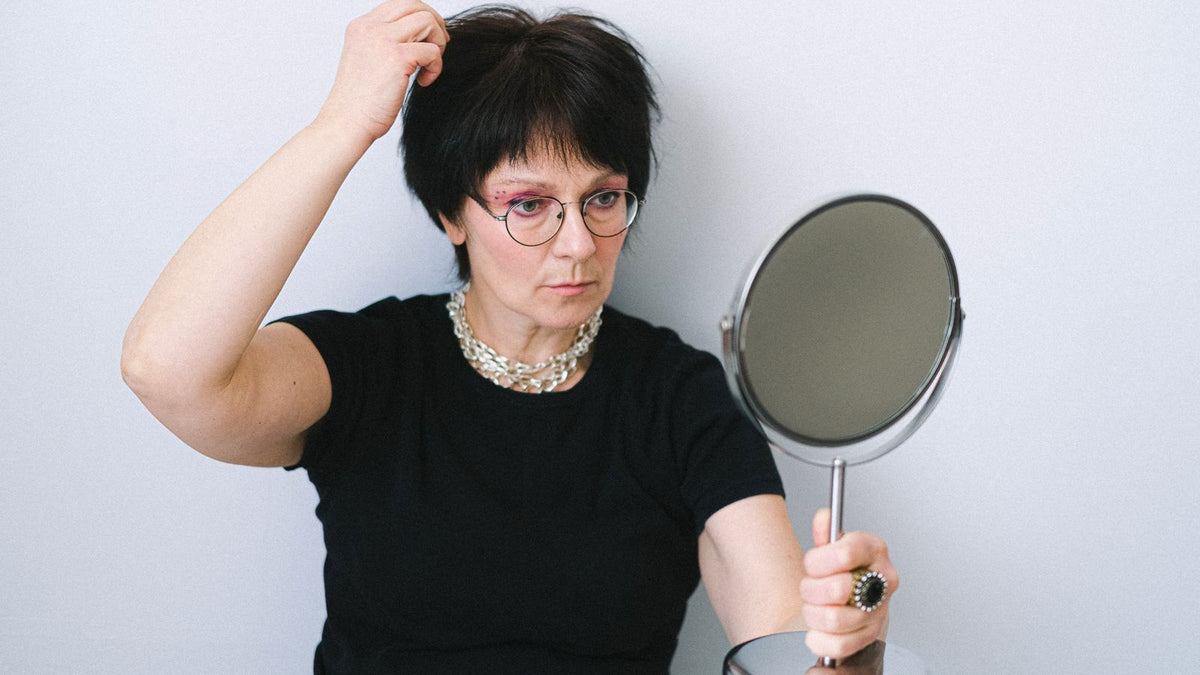 Woman checking her hair in a hand mirror at home before looking up trichologists Paisley on the professional registers