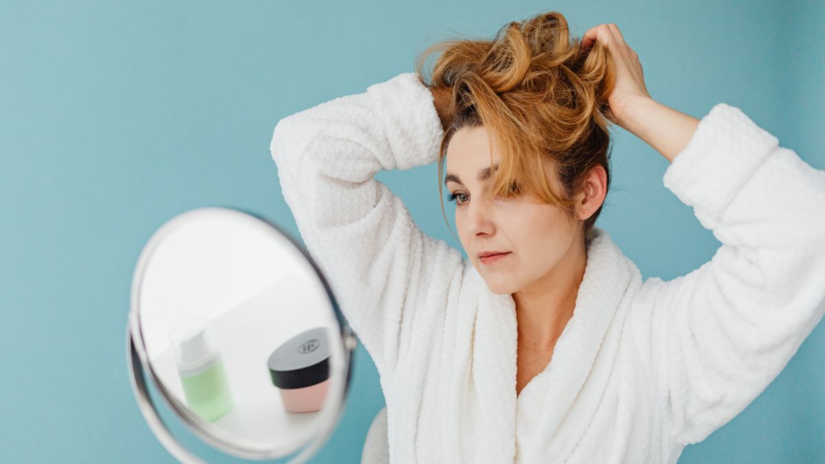 Woman in a bathrobe checking her fine hair in a mirror before searching for trichologists Swindon near me