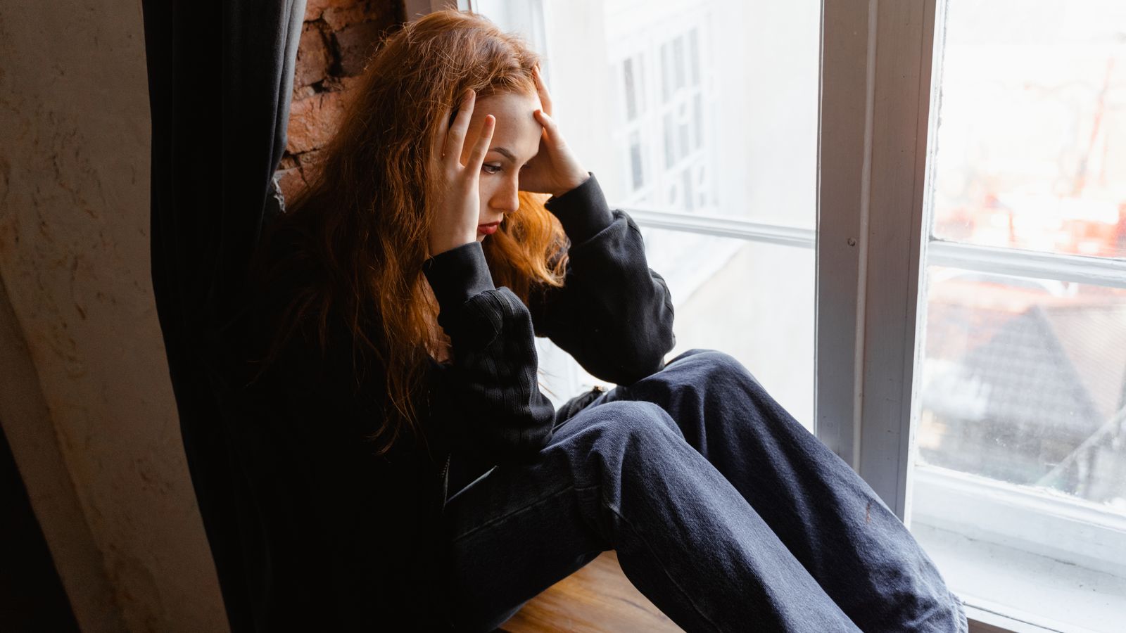 Thoughtful woman by a window reflecting on trichotillomania hair pulling