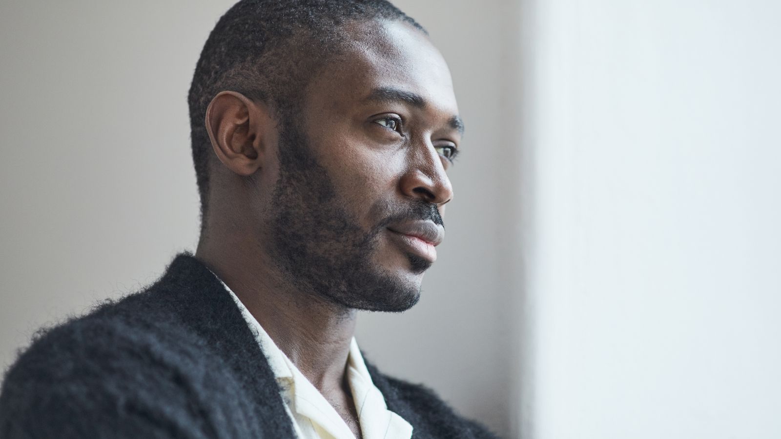 A thoughtful man gazing out of a window, considering what does DHT do in the body beyond hair