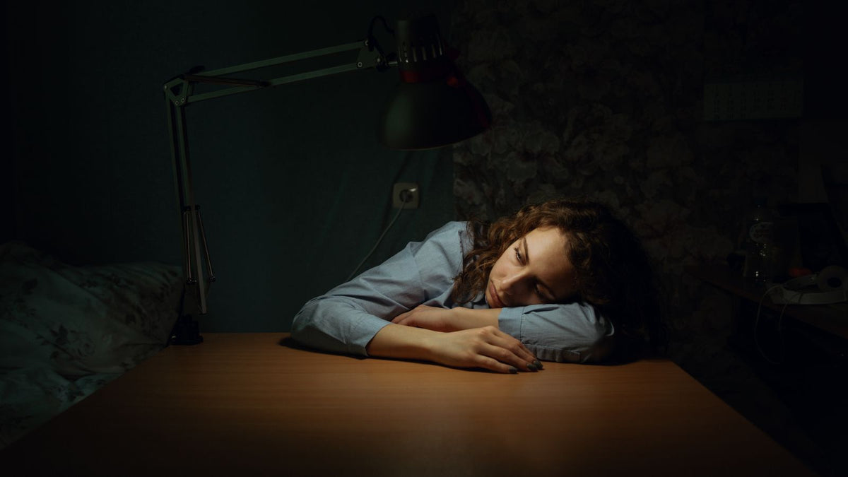 Tired woman resting her head on a desk, wondering how adrenal hormones and hair changes are linked